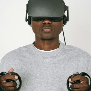 A man wearing VR glasses and gray sweater interacts with virtual reality controllers on a white background.
